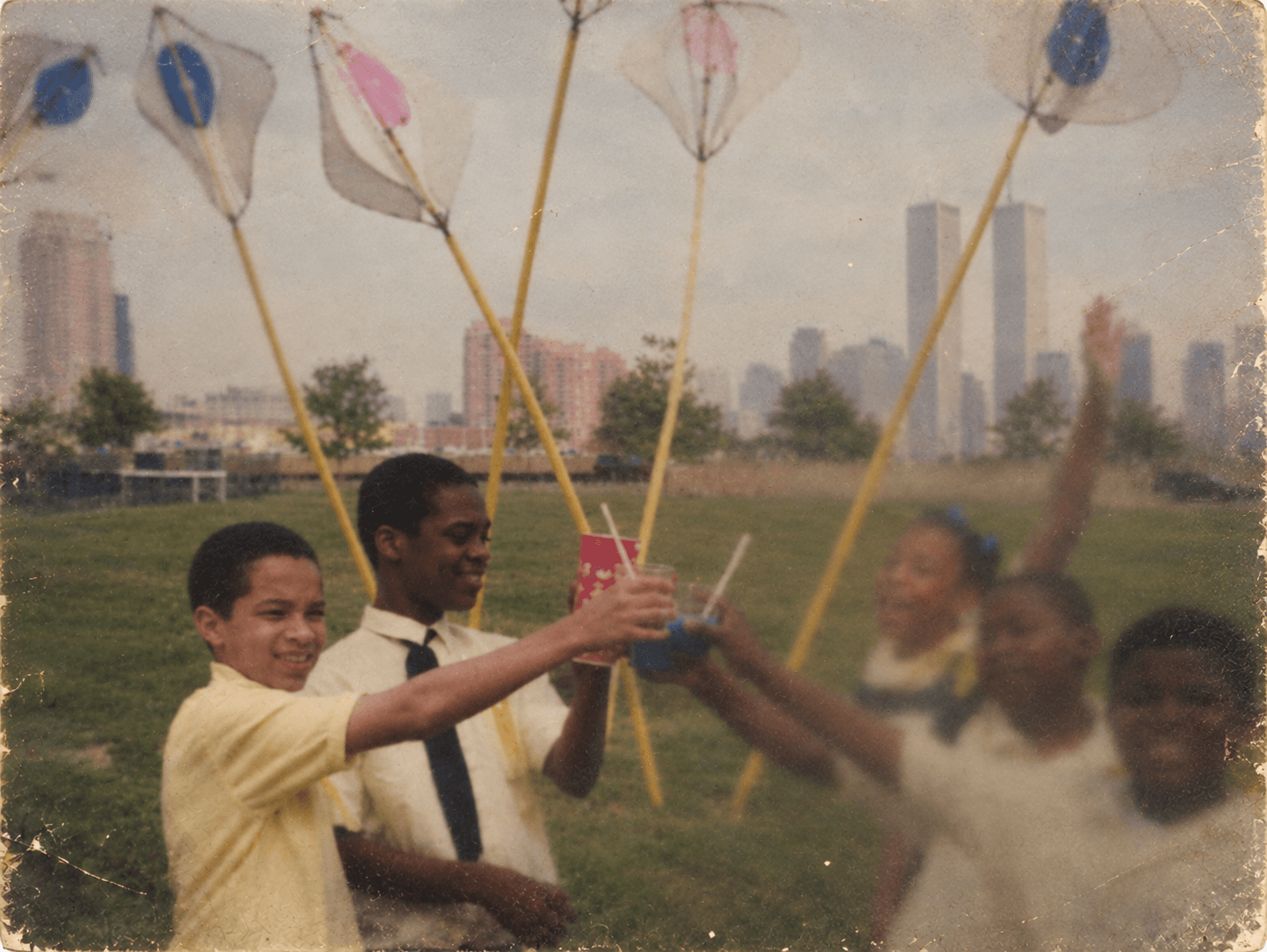 Children holding up cups and handmade nets in a park, with the lower Manhattan skyline behind them